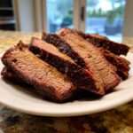 Slices of juicy Texas smoked brisket showing a visible smoke ring and dark bark, served on a white plate.